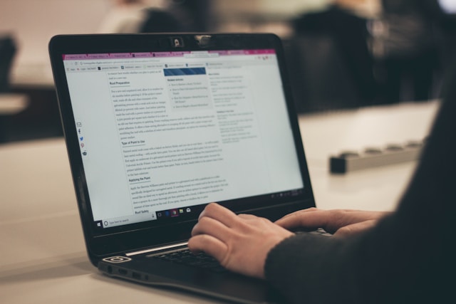 A person typing on a laptop with a webpage open, focused on reading or writing content in a quiet environment.